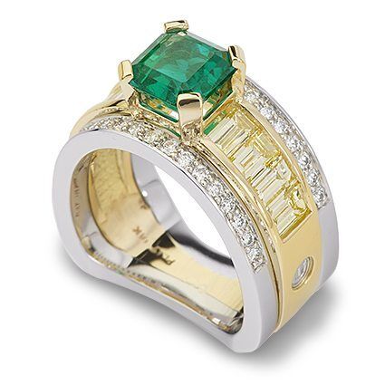 Emerald and diamond ring featuring a central green emerald stone, set in a two-tone gold band with baguette and round diamonds, showcasing luxury and craftsmanship.